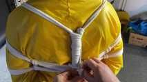 See Lady M, bound in shiny yellow Rainsuit, wearing a latex Mask and a Gasmask