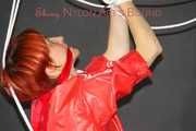 Sonja wearing a black rain pants and a red shiny nylon rain jacket tied and gagged with ropes overhead (Pics)