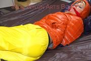 Pia tied and gagged on bed wearing a yellow rain pants and an orange downjacket (Pics)