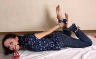 Emily in violet short-sleeve and jeans, hog-cuffed with steel cuffs, wiggles on the floor