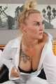 Busty blonde Frida posing in white shirt, leather corsage and black glossy leggins on bed
