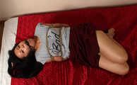Ballgagged barefoot Lois in grey t-shirt and red skirt, hogtied with hemp rope, rolls and wiggles on the mattress