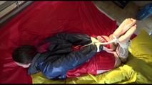 Jill tied and gagged on a bed wearing an sexy shiny nylon shorts and an oldschool rain jacket (Video)
