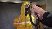 See Lady M, bound in shiny yellow Rainsuit, wearing a latex Mask and a Gasmask