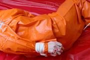 Pia tied and gagged in bed in a orange rainsuit and a red gag (Pics)