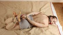 Topless ballgagged barefoot Amanda, hogtied with hemp rope, rolls on the mattress