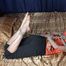 Barefoot Anne in pink tank-top and short black pants, hogtied with hemp rope, wiggles and rolls on the bed