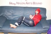 Jill tied, gagged and hooded infront of a sofa wearing a darkblue rain pants and a red rain jacket (Pics)