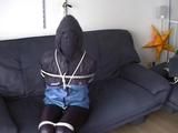 An archive girl tied, gagged and hooded two times on a sofa and chair wearing a shiny blue rainwear (Video)