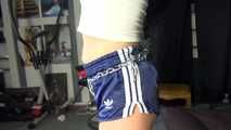 Watching sexy Sandra wearing an darkblue shiny nylon shorts and a white adidas top being tied and gagged overhead with ropes, chaines and a ballgag (Video)