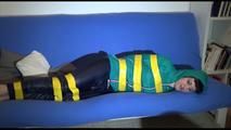 Mara tied, gagged and hooded with tape on a blue sofa wearing an blue/green rain combination (Video)
