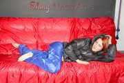 Sonja wearing a blue shiny nylon raver pants and a black down jacket posing and lollingn on the sofa (Pics)