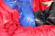 Sonja wearing a blue shiny nylon raver pants and a black down jacket posing and lollingn on the sofa (Pics)