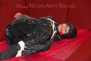 Lucy wearing a black shiny nylon rainh pants and a black down jacket tied and gagged on a sofa (Pics)