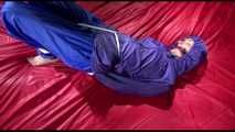 Sonja tied and gagged with ropes and a ballgag on a bed covered with a red shiny nylon cloth wearing a blue shiny nylon rain pants and a purple rain jacket (Video)