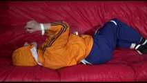 Lucy wearing a blue rain pants and an orange rain jacket being tied and gagged with belts on a sofa (Video)