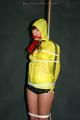 Alina tied and gagged to a pole in nylon shorts and yellow cagoule