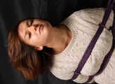 Barefoot Gwen in sweater and short skirt, suspended sideways with violet hemp rope, dangles in the air