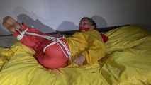 Watching Sandra  wearing an orange shiny nylon rain pants and a yellow shiny nylon rain jacket being tied and gagged on a bed with ropes and a clothgag (Video)