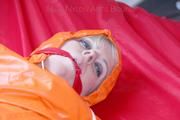 Pia tied and gagged in bed in a orange rainsuit and a red gag (Pics)