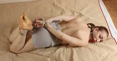 Topless ballgagged barefoot Amanda, hogtied with hemp rope, rolls on the mattress