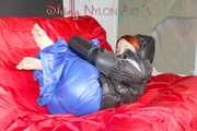 Sonja wearing a blue shiny nylon raver pants and a black down jacket posing and lollingn on the sofa (Pics)