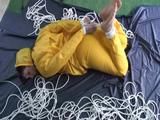 Archive girl tied and gagged on bed wearing a shiny yellow rainwear (Video)