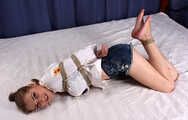 Barefoot Lisa in white shirt and jeans shorts, hogtied with hemp rope, wiggles and rolls on the bed