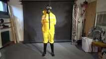 See Lady M, bound in shiny yellow Rainsuit, wearing a latex Mask and a Gasmask