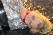 Pia tied and gagged with tape on a bed wearing a sexy silver rainwear combination (Pics) 