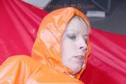 Pia tied and gagged in bed in a orange rainsuit and a red gag (Pics)