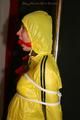 Alina tied and gagged to a pole in nylon shorts and yellow cagoule
