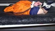 Lucy tied and gagged on a bed wearing a blue shiny nylon shorts and an orange shiny nylon rain jacket (Video)