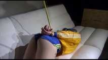 Mara with blue hairs wearing a sexy blue/yellow shiny nylon shorts and a yellow rain jacket tied and gagged with ropes and a ball gag on the sofa (Video)