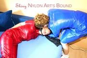 Leonie ties and gagges Stella on a sofa both wearing supersexy shiny nylon rainwear (Pics)