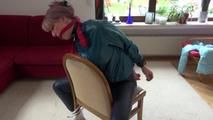 Mara tied and gagged on a chair with a bar wearing a sexy blue shiny nylon rain pants and a green rain jacket (Video)