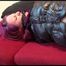 Mara tied and gagged on a sofa wearing a shiny black rain pants and down jacket (Video) 