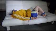 Mara with blue hairs wearing a sexy blue/yellow shiny nylon shorts and a yellow rain jacket tied and gagged with ropes and a ball gag on the sofa (Video)