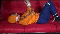 Lucy wearing a blue rain pants and an orange rain jacket being tied and gagged with belts on a sofa (Video)