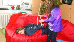 Leonie tied and gagged by Stella on a sofa both wearing sexy shiny nylon rainwear (Pics)