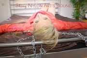 Mara tied and gagged with chains and cuffs on a bed wearing a superhot yellow shiny nylon shorts and an orange rain jacket (Pics)