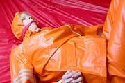 Pia tied and gagged in bed in a orange rainsuit and a red gag (Pics)