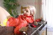 Mara tied and gagged with chains and cuffs on a bed wearing a superhot yellow shiny nylon shorts and an orange rain jacket (Pics)