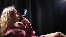 Blonde girl is smoking a cigarette is the dark room