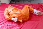 Pia tied and gagged in bed in a orange rainsuit and a red gag (Pics)