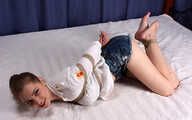 Barefoot Lisa in white shirt and jeans shorts, hogtied with hemp rope, wiggles and rolls on the bed