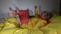 Watching Sandra  wearing an orange shiny nylon rain pants and a yellow shiny nylon rain jacket being tied and gagged on a bed with ropes and a clothgag (Video)