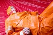 Pia tied and gagged in bed in a orange rainsuit and a red gag (Pics)