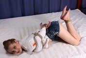 Barefoot Lisa in white shirt and jeans shorts, hogtied with hemp rope, wiggles and rolls on the bed