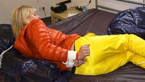 Pia tied and gagged on bed wearing a yellow rain pants and an orange downjacket (Pics)
